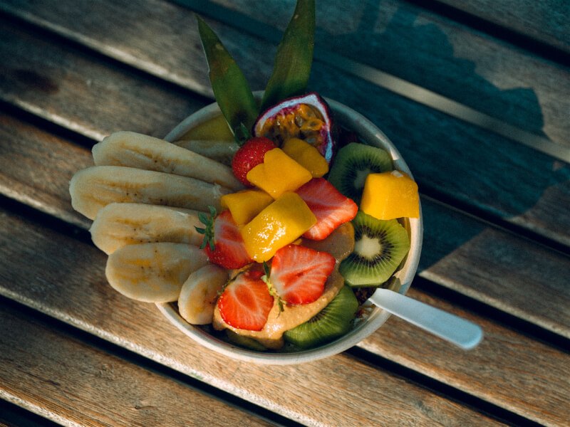 tigela branca com salada de frutas mistas e colher sobre fundo de madeira