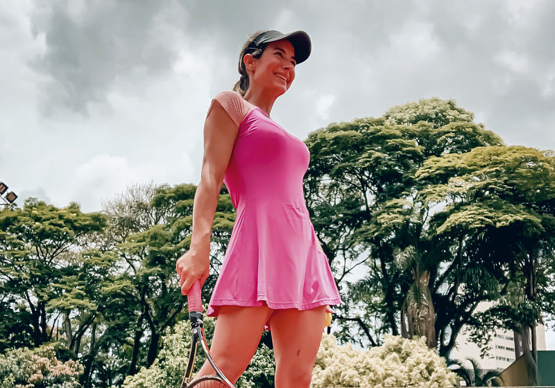 mulher de macaquinho saia fitness rosa e boné para jogar beach tennis