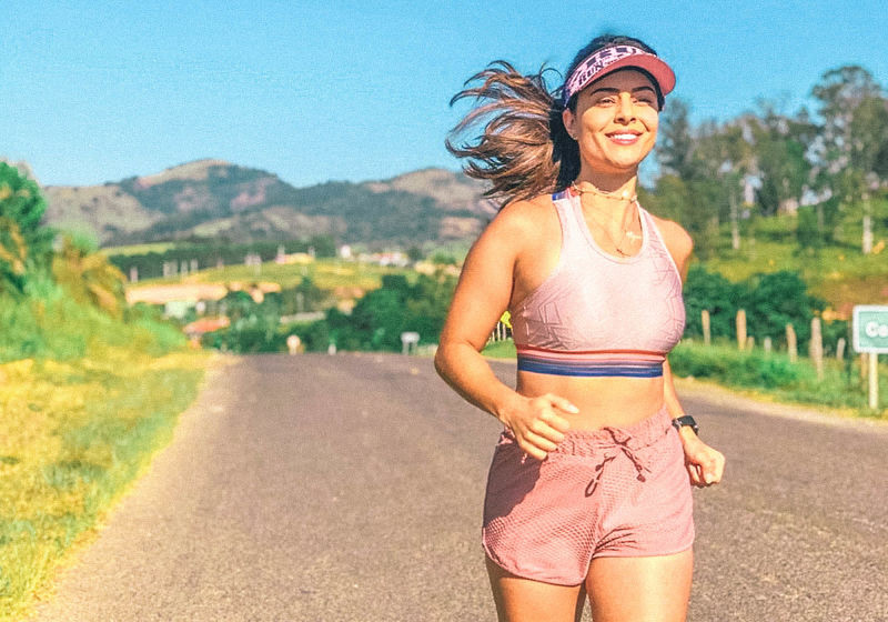 mulher correndo sorrindo usando roupa fitness rosa claro