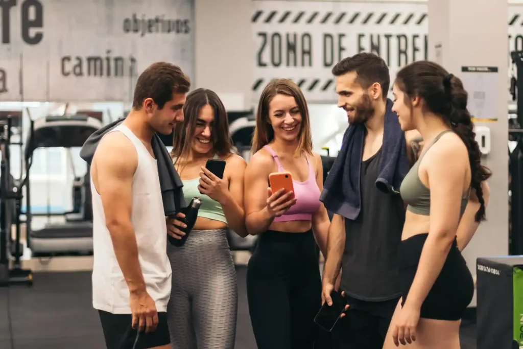 Grupo de pessoas em academia sorrindo e olhando o celular, lendo frases para loja fitness que geram conexão e engajamento