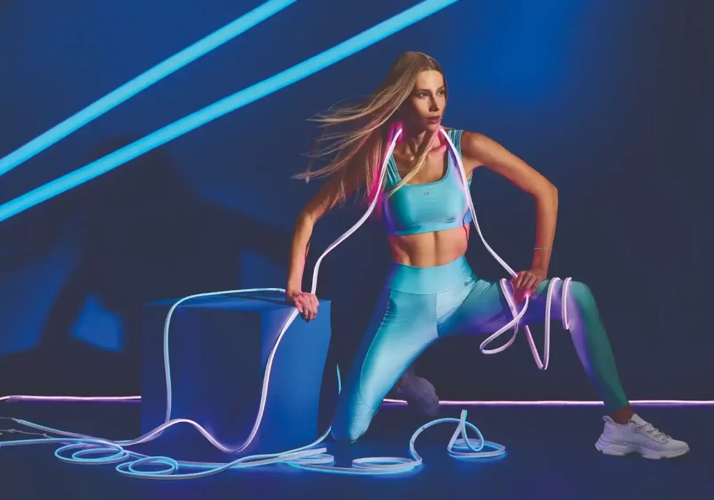 Modelo em roupas esportivas azuis iluminada por neon, reforçando a paleta de cores em loja fitness.