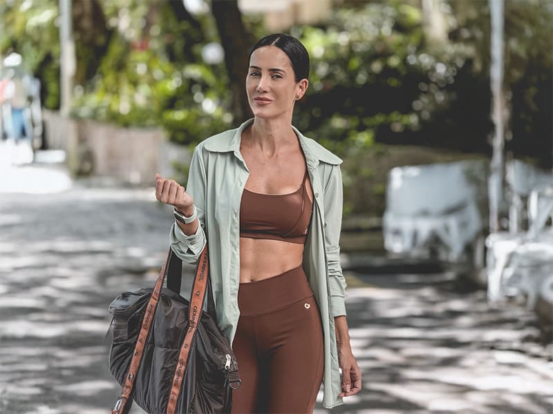 Mulher de roupas de ginástica segurando bolsa.