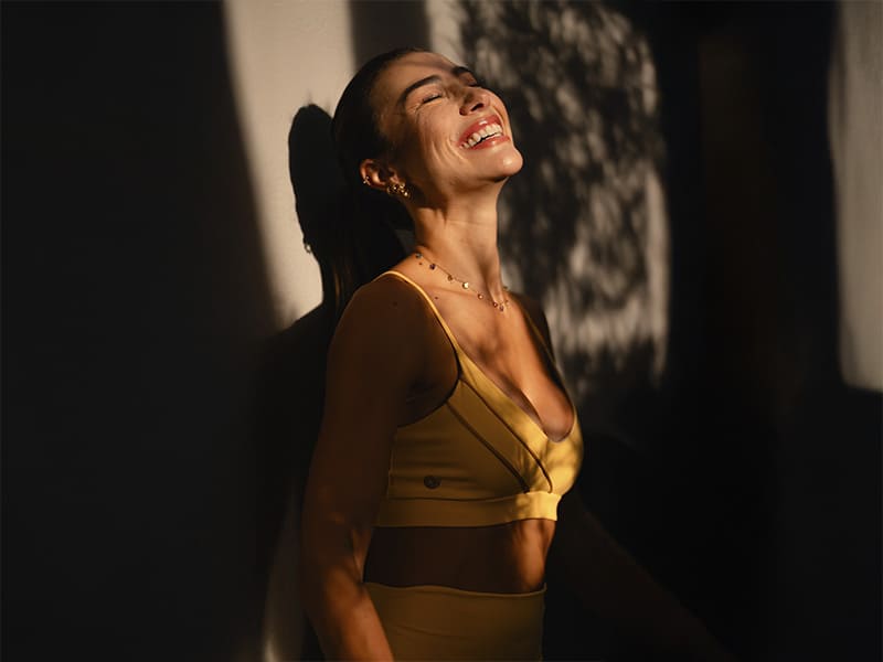 Mulher sorridente em vestido amarelo com sombras ao fundo.